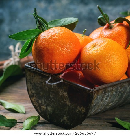 Tangerines with leaves and cinnamon stick on old wooden table. Square image, selective focus