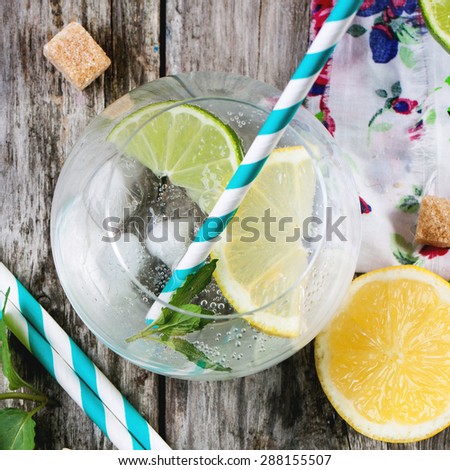 Fresh homemade lemonade with lemon, lime and mint in glasses with vintage cocktail tube over wooden table. Top view. Square image.