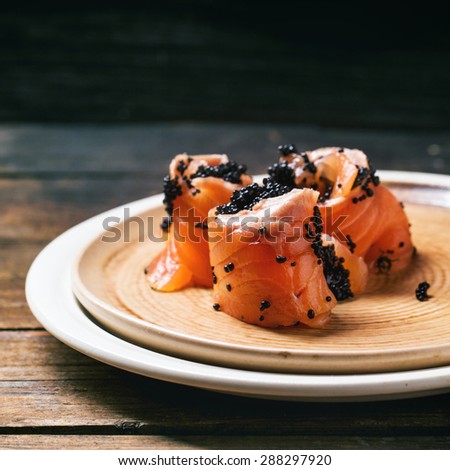 Salmon rolls with black caviar, served on ceramic plate on old wooden table. Square image