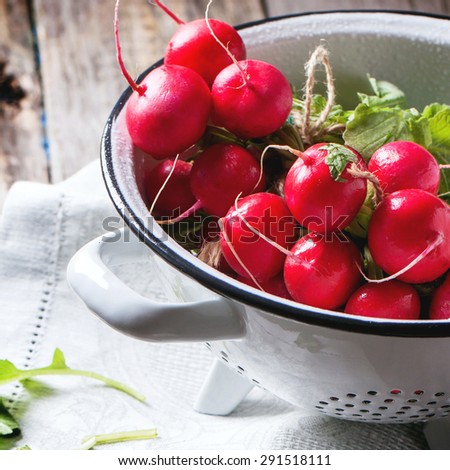 Fresh wet radishes in white colander over old wooden table. Square image with selective focus