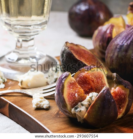 Figs with blue cheese, white wine and crackers on wooden cutting board. Square image with selective focus.
