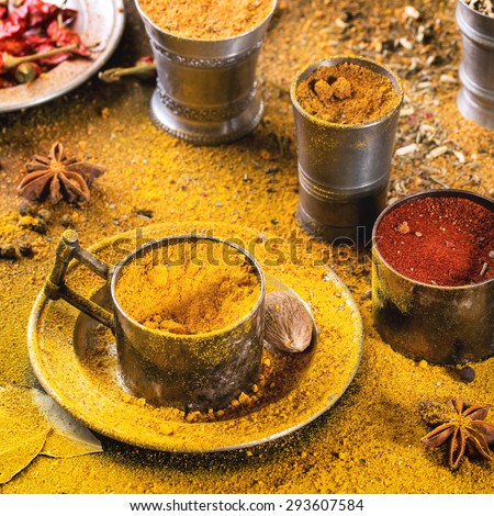 Set of spices pepper, turmeric, anise, coriander in vintage metal cups over yellow curry powder. Square image with selective focus.