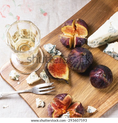 Figs with blue cheese, white wine and crackers on wooden cutting board. Top view. Square image with selective focus.