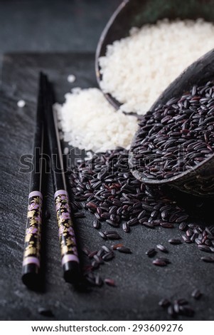 Black and white rice in old metal china bowls with black chopsticks over black slate background.