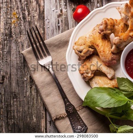 Top view on plate of grilled chicken wings served with fresh basil over old wooden table. Top view. Square image