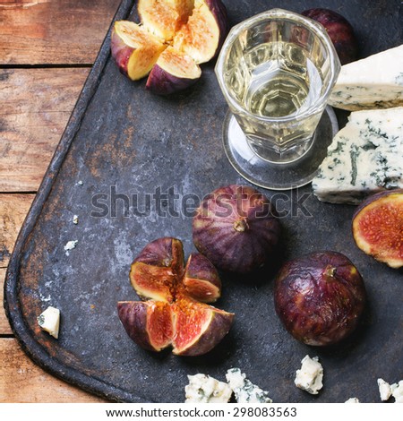Figs with blue cheese, white wine and crackers on black cutting board. Top view. Square image