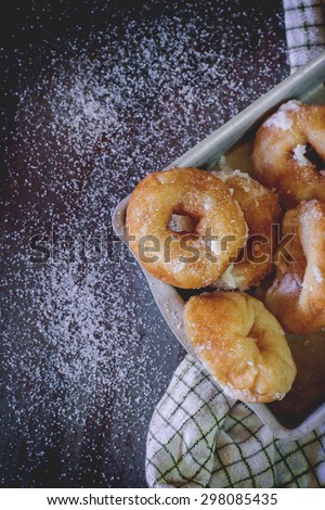 Homemade donuts with sugar and sugar powder in aluminum tray on checkered kitchen towel. Old metal background. Natural day light. Top view.  With copyspace on left.