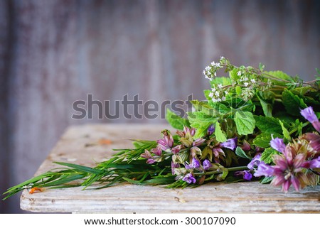Assortment of fresh herbs mint, oregano, thym, blooming sage over old wooden background. Natural day light. With copyspace on top