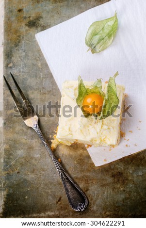 Piece of homemade sliced cake with creamy mousse and tropical fruits mango and physalis over metal background with vintage fork. Top view