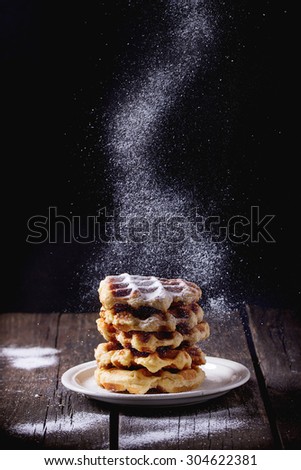 White plate with homemade belgian waffles with Sifting sugar powder over black background. sugar powder over old wooden table. Dark rustic style.