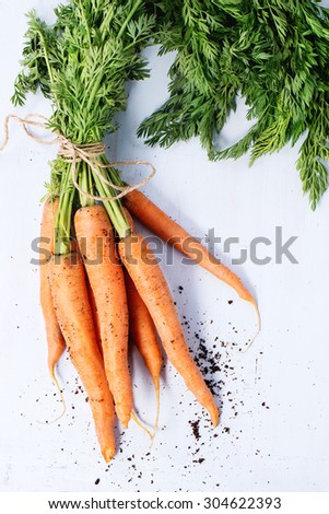 Bundle of carrots with soil over light blue wooden background. Top view