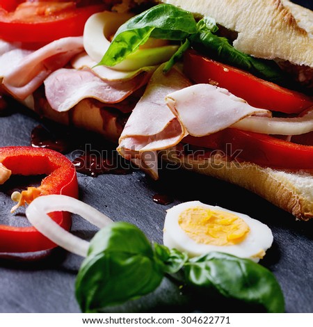 Sandwich with ham, eggs, vegetables and ketchup over black background. Square image