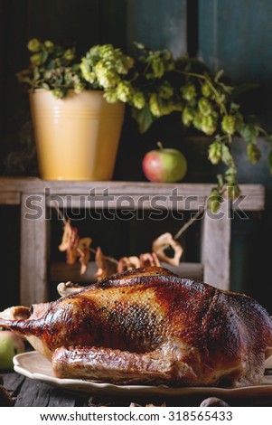 Roast stuffed goose on ceramic plate with ripe apples over wooden kitchen table. Dark rustic style.