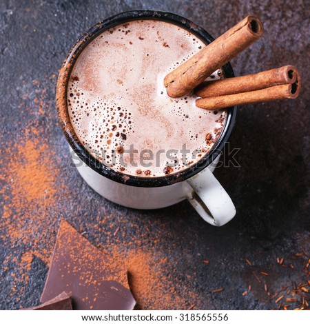 Vintage mug of hot chocolate with cinnamon sticks over dark background. Square image with selective focus