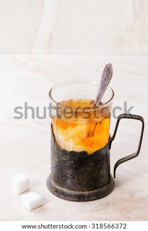 Milk dissolves in retro cup of hot tea in vintage glass-holder with tea spoon and sugar cubes over white marble backgtound.