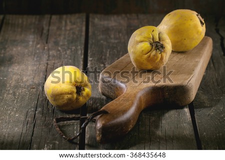 Three whole juicy quinces on old chopping board over wooden table in sunlight. Dark rustic style.