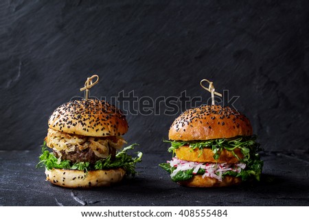 Homemade traditional and veggie burgers with beef, fried onion, sweet potato, radish and pea sprouts, served over black textured background. Healthy vs unhealthy concept food. Copy space