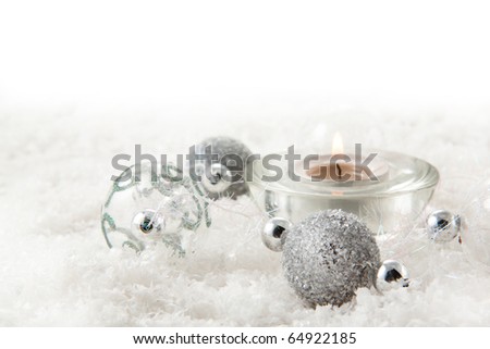 Silver christmas balls with and burning candle on the snow