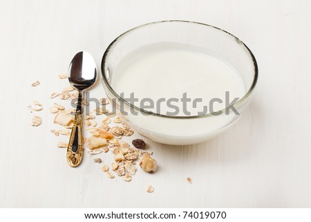 Bowl of yogurt with muesli and silver spoon on white table