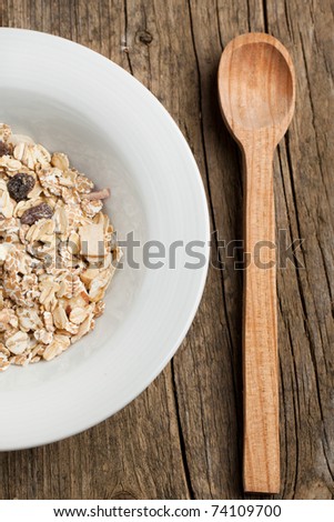 Plate with dry muesli and wooden spoon on old wooden desk