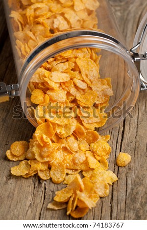 Golden corn flakes from plastic jar on old wooden table