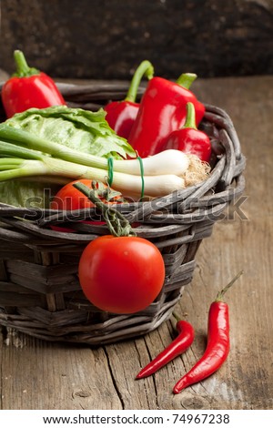 Tomato, green onion, green salad, red paprika and red hot chili peppers in basket on old wooden table. See series