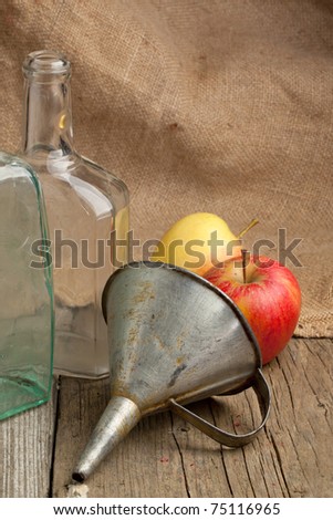 Composition with tow vintage bottles, fresh apples and old metal funnel on old wooden table with sacking as background