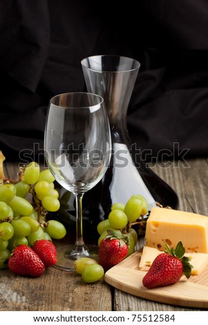 Red wine in decanter with grapes, strawberries and cheese on old wooden table