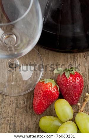 Empty glass near red wine in decanter with grapes and strawberries on old wooden table