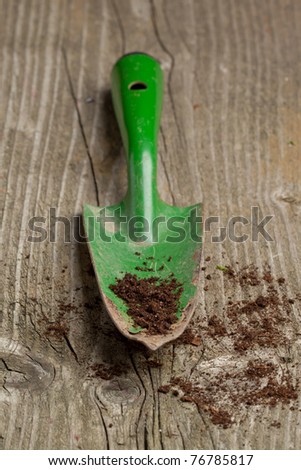 Green garden spade with ground on old wooden desk