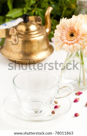 Bunch of gerbera flower with empty glass cup and old golden teapot on white table