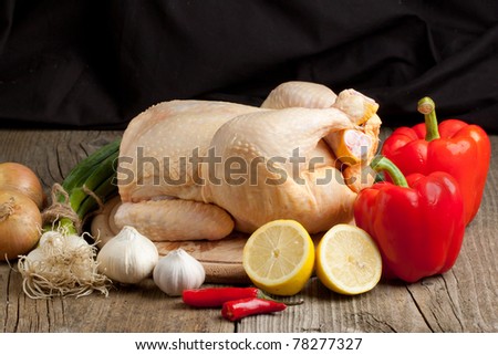 Composition with raw chicken, onion, garlic, red paprika and lemon on old wooden table