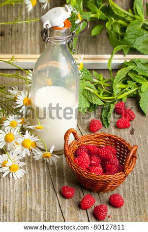 Still-life with basket of fresh ripe raspberries, bottle of milk and bunch of camomile flowers on old wooden table