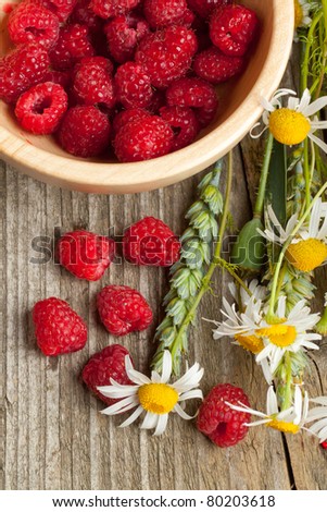 Background with fresh ripe raspberries and camomile flowers on old wooden table