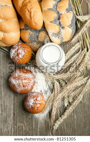 Top view on lot of bread and cakes with jug of milk and spikes of rye