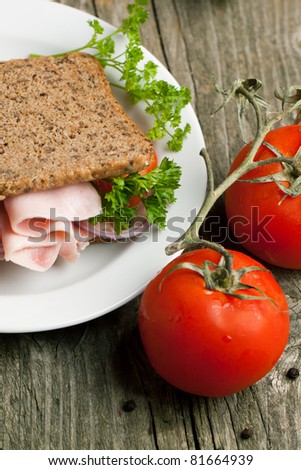 White plate with fresh sandwich with cheese, ham and tomato and tow fresh tomatoes on old wooden table