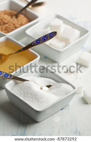 Various of white and brown sugar and honey in white plates on white wooden table