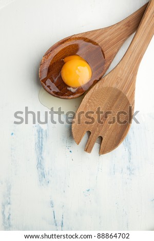 Broken egg in wooden spoon on white table