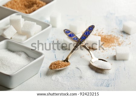 Various of white and brown sugar in dessert spoons on white wooden table