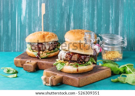 Two hamburgers with beef burger cutlet, fried onion, spinach, ketchup sauce and blue cheese in traditional buns, served on wood chopping board over bright turquoise background. Copy space