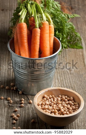 Metal bucket of freshly washed whole carrots and wooden bowl of chickpeas on old wooden table