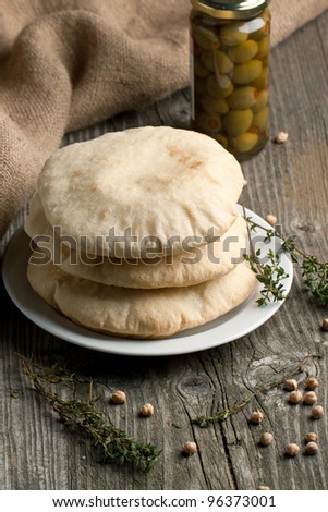 Plate with fresh pitas bread, thyme and glass jar of olives on old wooden table