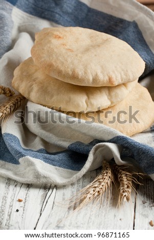 Fresh pitas bread with ears of rye and wheat on white wooden table