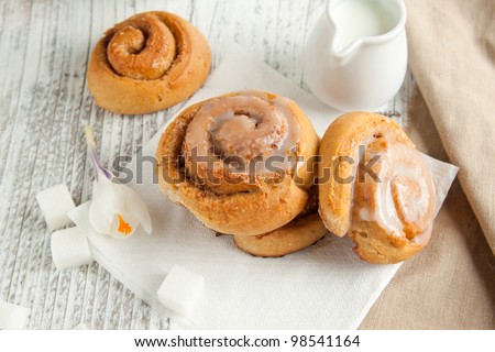 Sweet cinnamon buns with sugar and milk on white wooden table