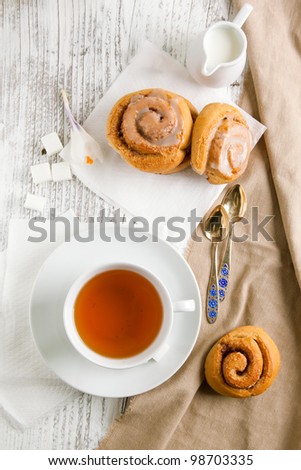 Breakfast with sweet cinnamon buns and cup of tea served on white wooden table
