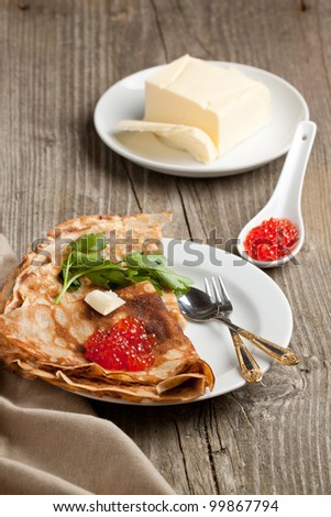 Tot view on pancakes with spoon of red caviar and twig of parsley served on old wooden background