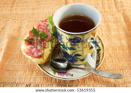 image of a cup of tea and a sandwich with sausage on jute napkin