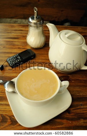 Break for tea in cafe. A cup of tea, sugar bowl, spoon, teapot and cellphone on the table.