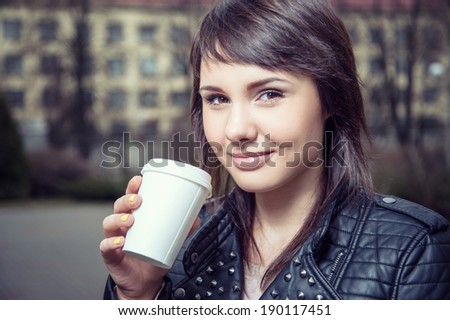 Beautiful young woman is drinking coffee outdoors. Invigorating morning. Stylish look