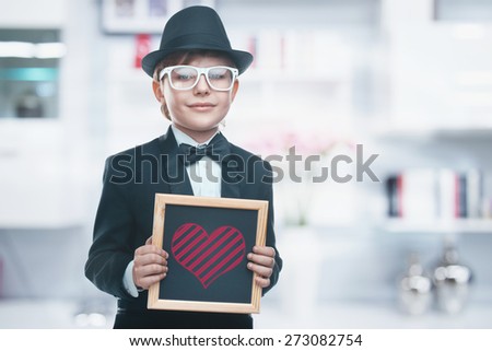 Beautiful little boy with a board. Looking at the camera. Drawing a heart. Valentine\'s day holiday